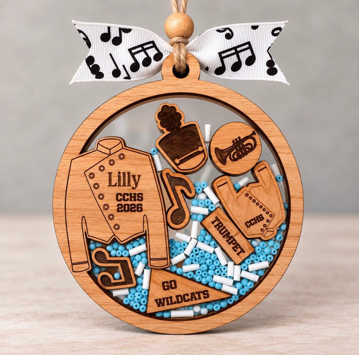Round wooden marching band shaker ornament with a uniform, trumpet, and music notes, beads in school colors, and the name, school, and year