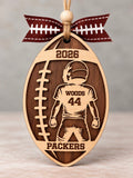 Wooden football shaped ornament with a youth player, jersey number, last name, team name, and year, tied with a football ribbon