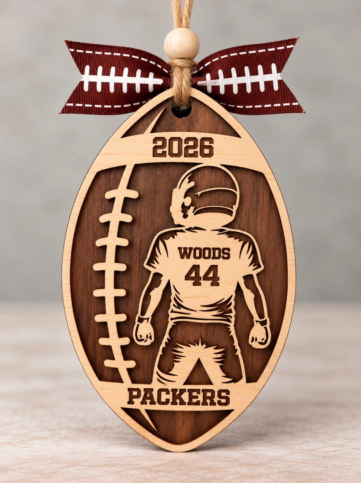Wooden football shaped ornament with a youth player, jersey number, last name, team name, and year, tied with a football ribbon