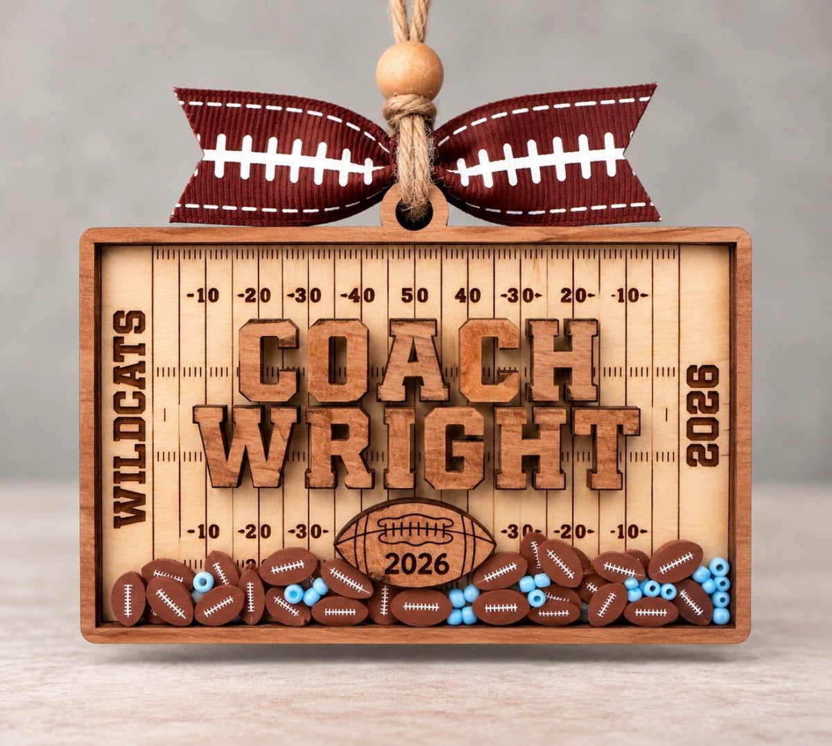 Wooden football field shaker ornament with a coach's name, team name, and year, filled with football beads in school colors