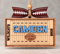 Rectangular wooden football field ornament with yard lines, a name in blue, team name, and year, tied with a football ribbon