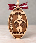 Wooden football shaped ornament with a cheerleader silhouette, her first name, team name, and year, tied with a football ribbon
