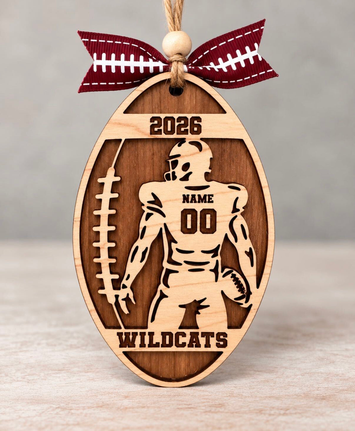 Layered wood football ornament with a football player, jersey number, last name, team name, and year, tied with a football ribbon
