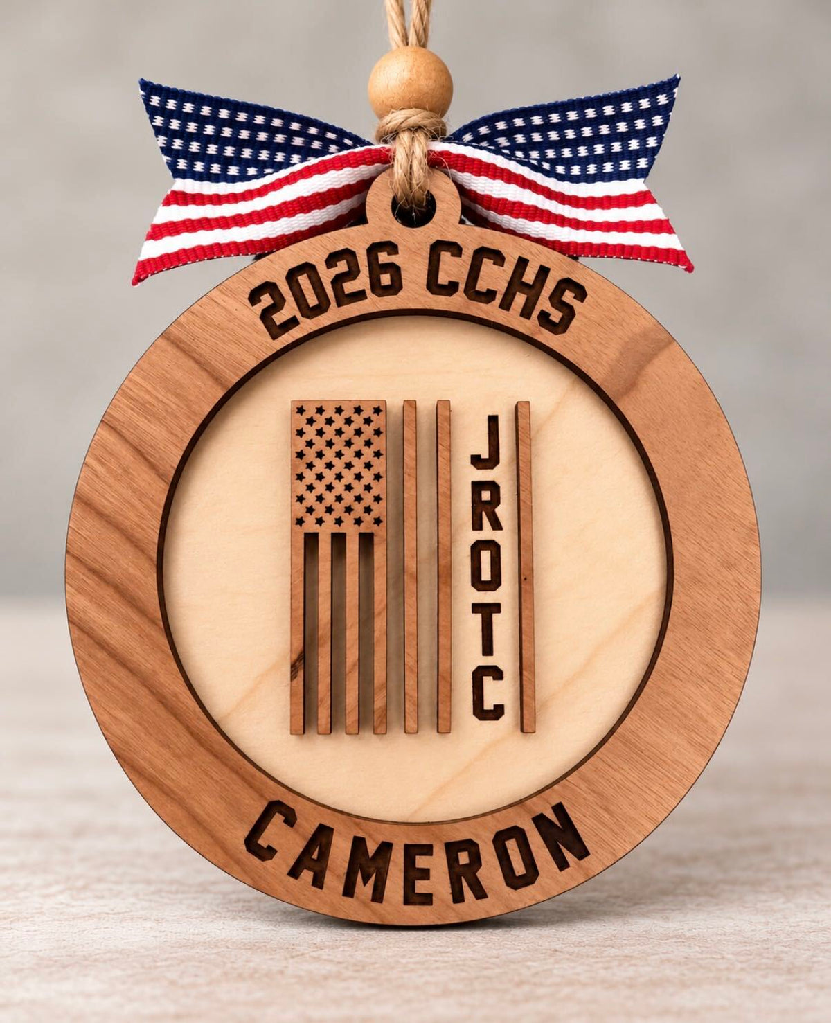 Round layered wood JROTC ornament with an American flag design and the cadet's name, school, and year, tied with a flag ribbon