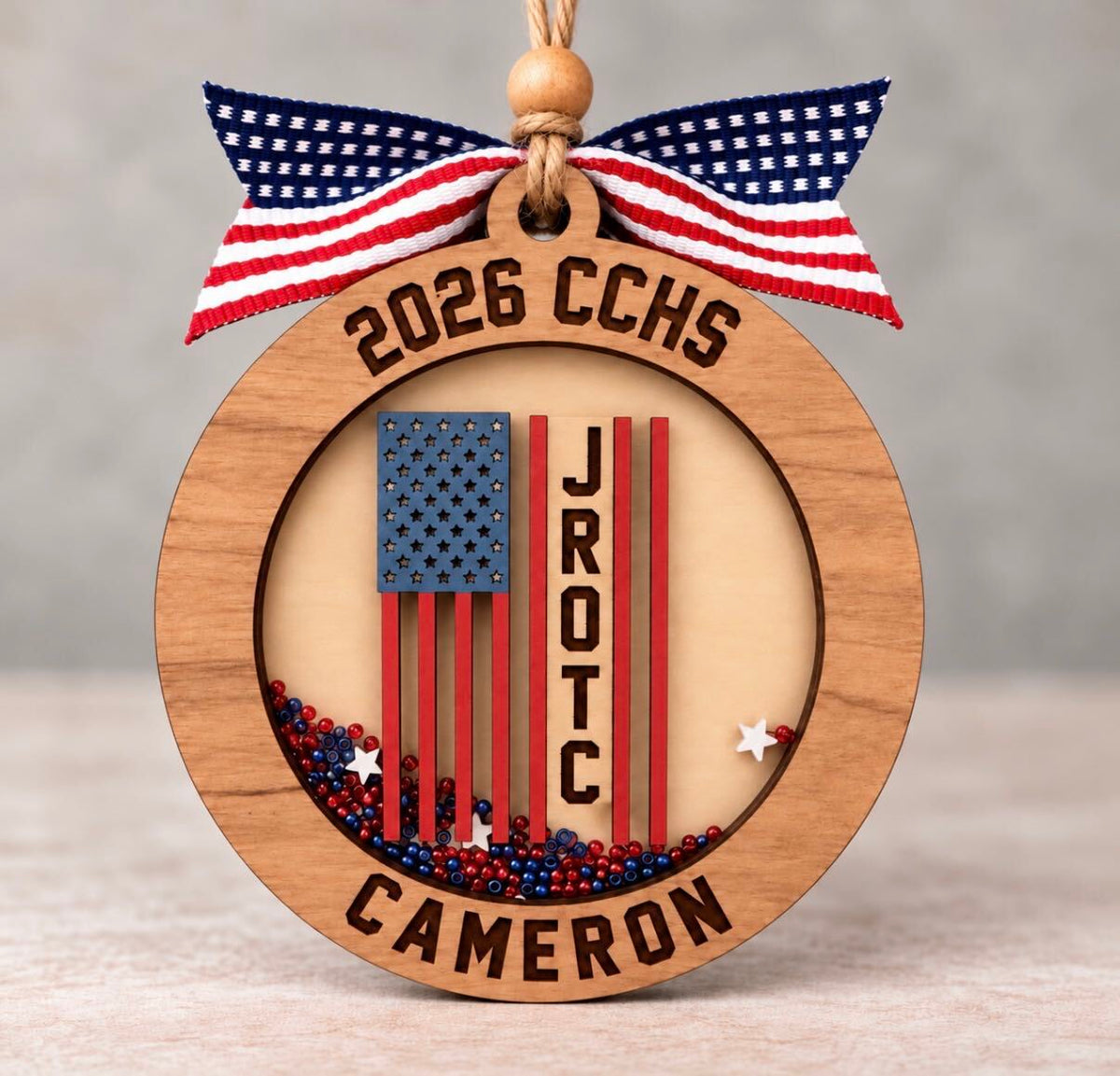 Round wooden JROTC shaker ornament with an American flag, red, white, and blue beads, and the cadet's name, school, and year